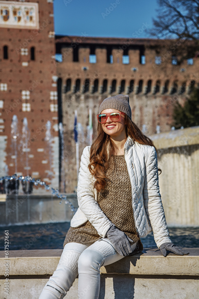 Rediscovering things everybody love in Milan. smiling trendy woman in front of Sforza Castle in Milan, Italy sitting near fountain