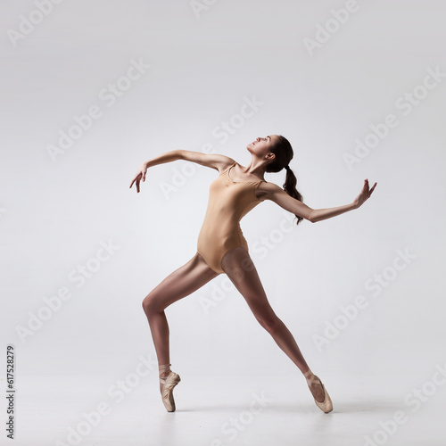 Fototapeta Naklejka Na Ścianę i Meble -  young beautiful ballet dancer in beige swimsuit posing on pointes on light grey studio background