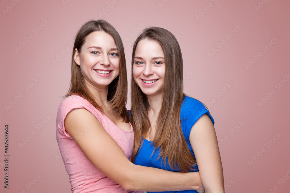 Studio portait of young and happy twin sisters embracing Studio portait of young and happy twin sisters embracing