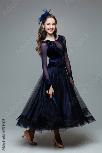 Beautiful teenager ballroom dancer with long blond hair in long dark blue dress. Studio portrait on grey background. Copy space.