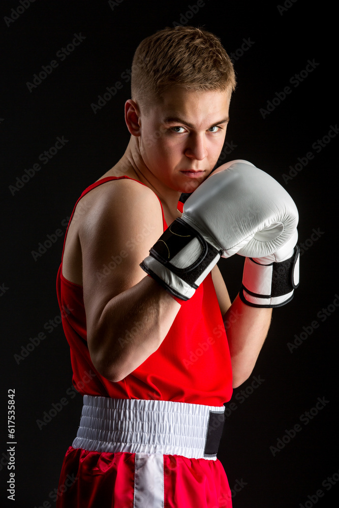 Young handsome boxer sportsman in red boxer suit and white gloves standing on black backgound. Copy space.