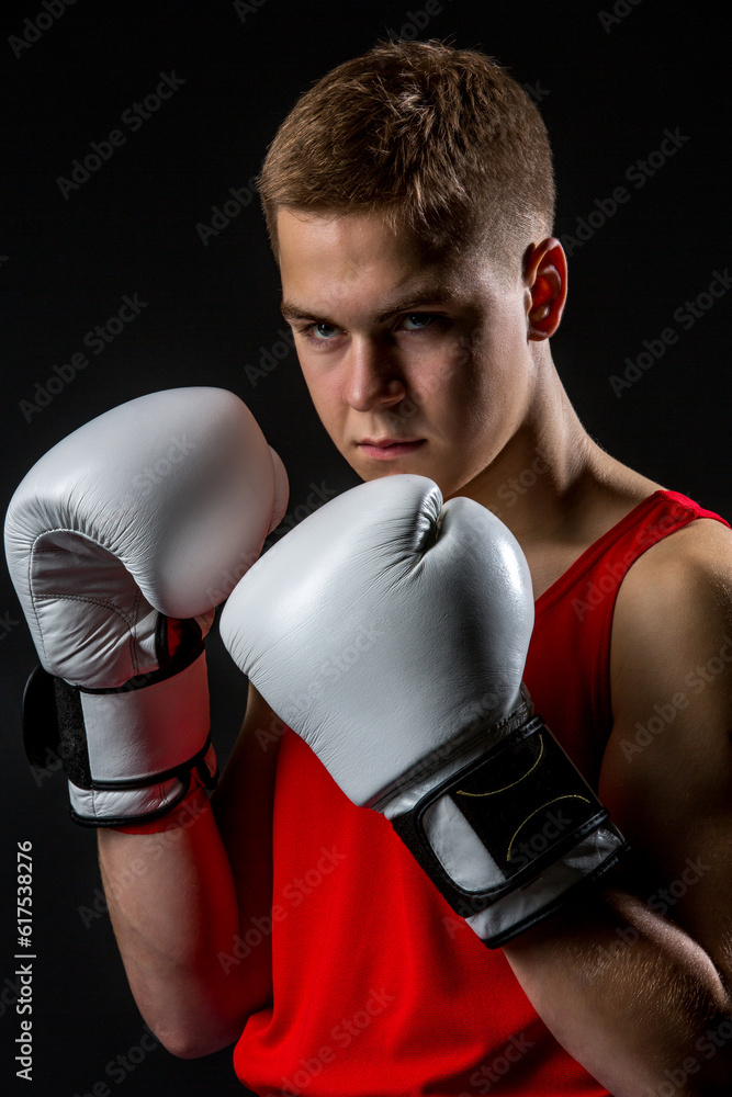 Young handsome boxer sportsman in red boxer suit and white gloves standing on black backgound. Copy space.