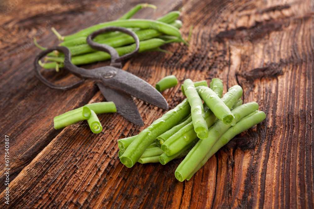 Raw fresh green beans with water drops on brown wooden textured table. Fresh vegetable eating. Raw fresh green beans with water drops on brown wooden textured table. Fresh vegetable eating.
