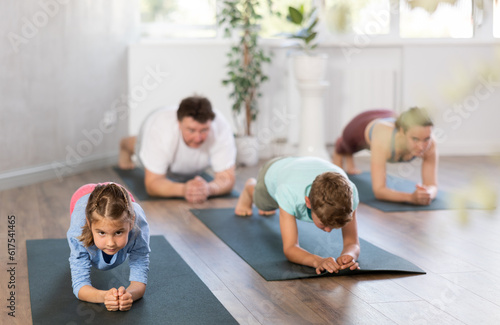Parents together with children in yoga pose upward-facing dog at gym