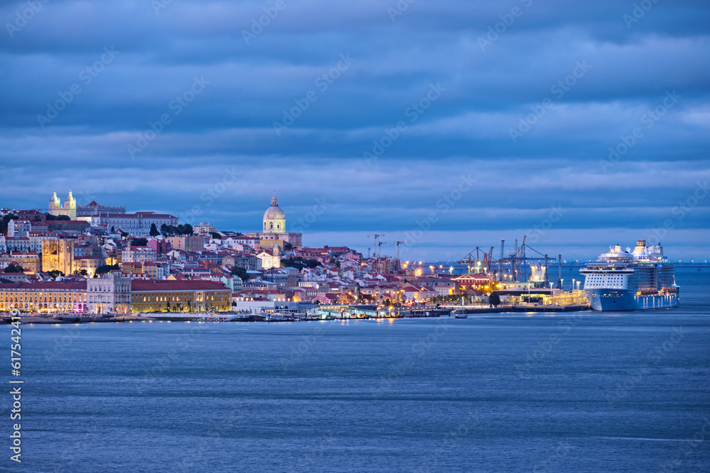 View of Lisbon over Tagus river with passing ferry boat from Almada with moored cruise liner in evening twilight. Lisbon, Portugal