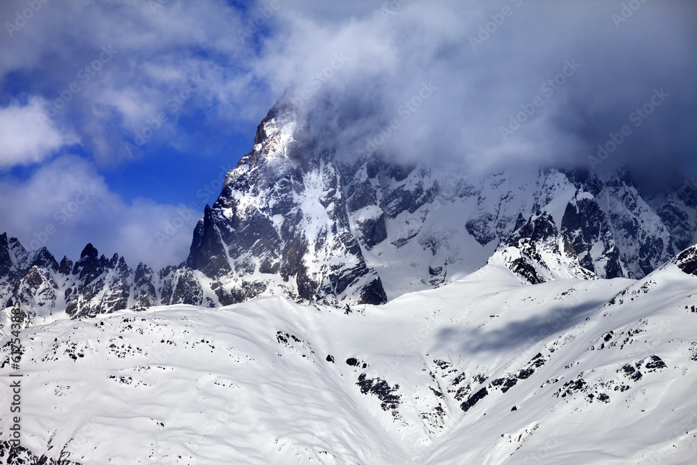 Mount Ushba in fog at sun winter day before storm. Caucasus Mountains. Svaneti region of Georgia. Mount Ushba in fog at sun winter day before storm. Caucasus Mountains. Svaneti region of Georgia.