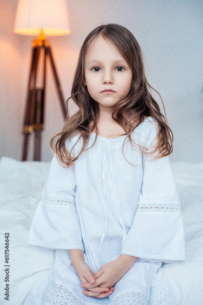 Cute little girl wearing nightgown sitting on the bed in bedroom ...