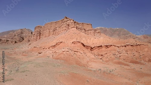 Flying forward and upward through the Kitchen Mountain in the red desert canyon, revealing a view of distant mountains. Aerial panoramic view