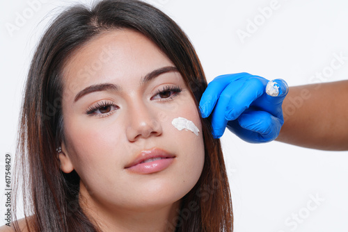 Plastic surgery concept. Close up photo of young woman with glowing skin and hands in blue medical gloves marking facial surgery on women face.