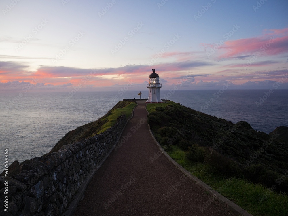Pedestrian asphalt road walkway leading to historic white Cape Reinga lighthouse on cliff top in Northland New Zealand