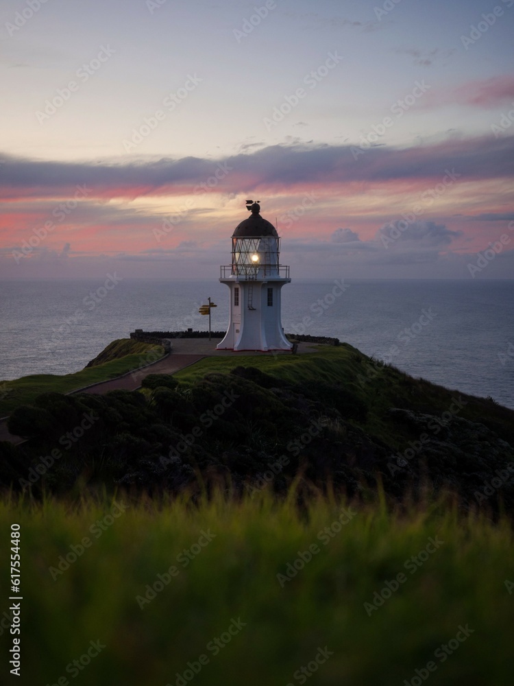 Panoramic view of historic white Cape Reinga lighthouse landmark on oceanside clifftop during sunset in New Zealand
