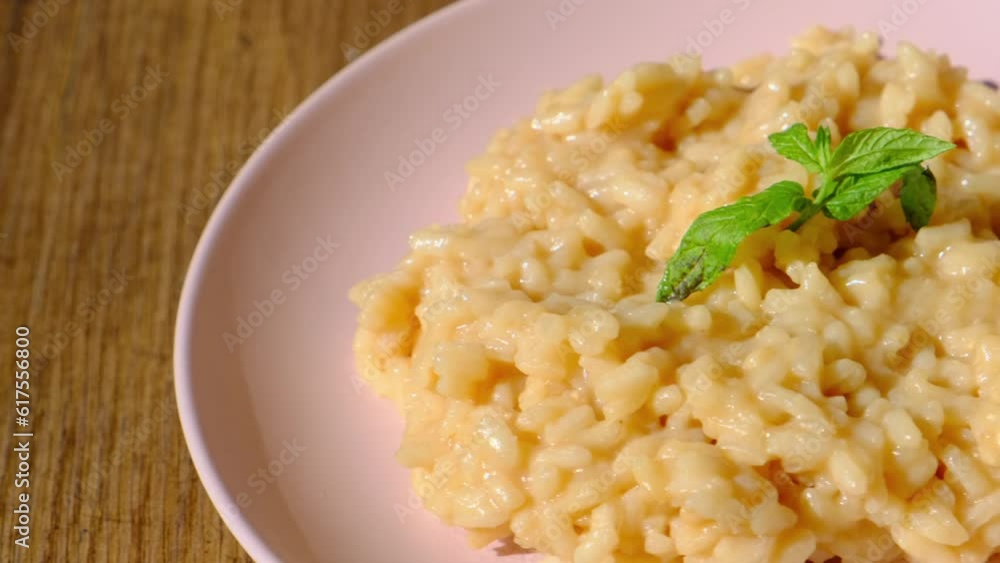 Risotto pilaf with parmesan cheese on pink plate on wooden background,slow motion Risotto pilaf with parmesan cheese on pink plate on wooden background,slow motion