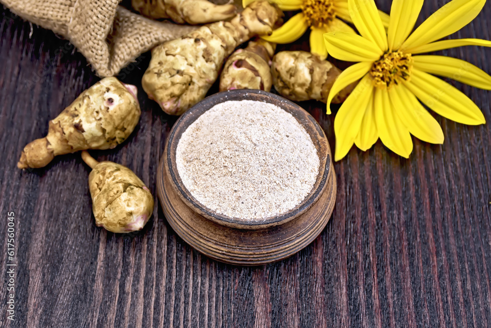 Flour of Jerusalem artichoke in a clay bowl with a flower and vegetables on a wooden boards background Flour of Jerusalem artichoke in a clay bowl with a flower and vegetables on a wooden boards background