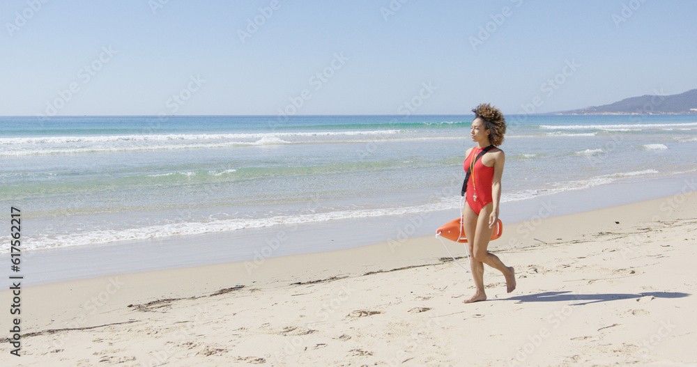 Lifeguard female wearing red swimsuit with rescue float walking along beach. Tarifa beach. Provincia Cadiz. Spain.