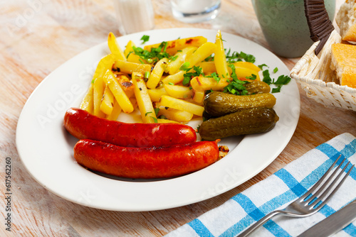 Traditional German cuisine. Baked frankfurters with fried potatoes and marinated gherkins