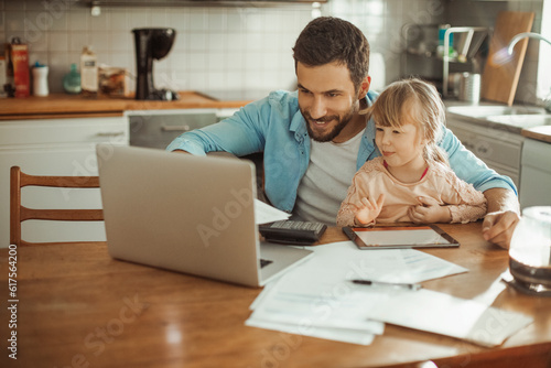 Single father using the laptop with his young daughter in his lap