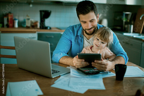 Single father using a digital tablet with his daughter in the morning while going over bills