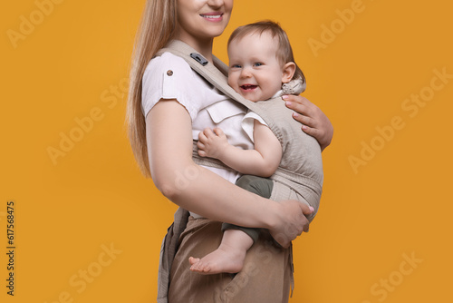 Mother holding her child in sling (baby carrier) on orange background, closeup