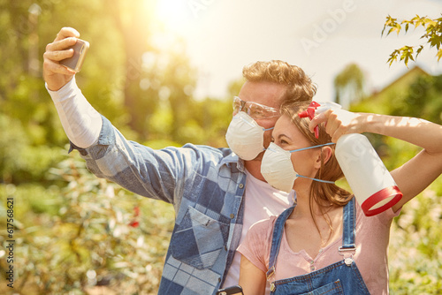 Male and female professional gardeners posing for selfie with sprayers and respirators while fertilizing plants in hothouse. © Designpics
