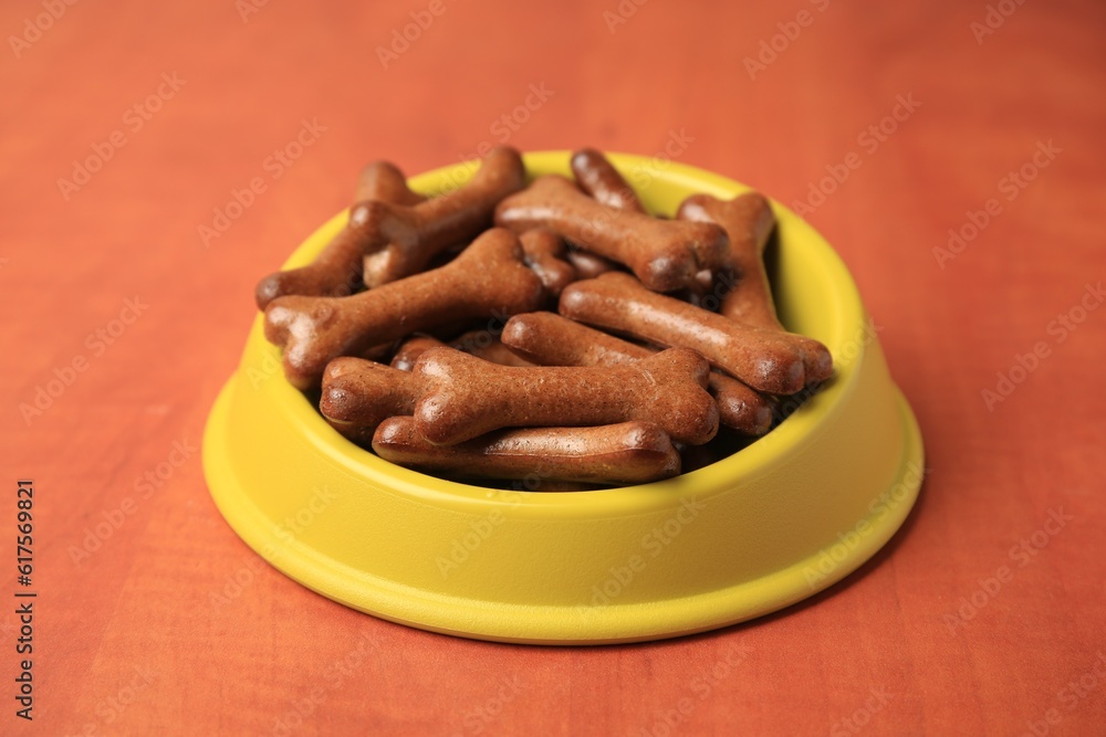 Yellow bowl with bone shaped dog cookies on wooden table, closeup Yellow bowl with bone shaped dog cookies on wooden table, closeup