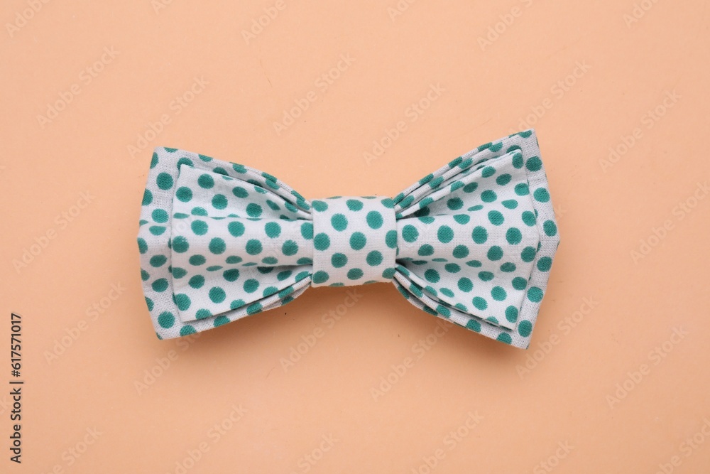 Stylish white bow tie with green polka dot pattern on pale orange background, top view Stylish white bow tie with green polka dot pattern on pale orange background, top view