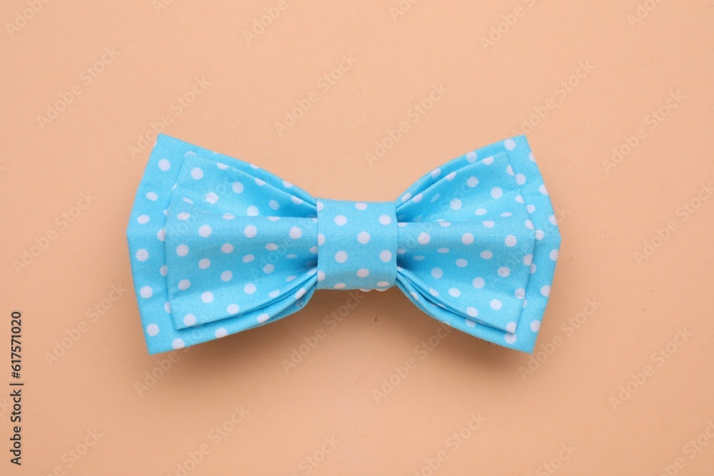 Stylish light blue bow tie with polka dot pattern on pale orange background, top view Stylish light blue bow tie with polka dot pattern on pale orange background, top view