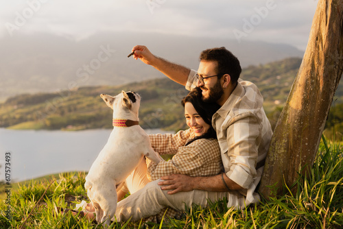 smiling couple playing with their pet at the sunset by a tree