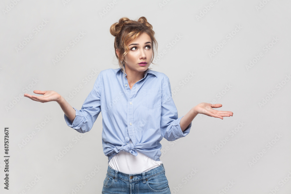 Who knows. Clueless hesitant beautiful blonde woman spreads palms sideways shrugs shoulders has indecisive expression, looking away, wearing blue shirt. Indoor studio shot isolated on gray background. Who knows. Clueless hesitant beautiful blonde woman spreads palms sideways shrugs shoulders has indecisive expression, looking away, wearing blue shirt. Indoor studio shot isolated on gray background.