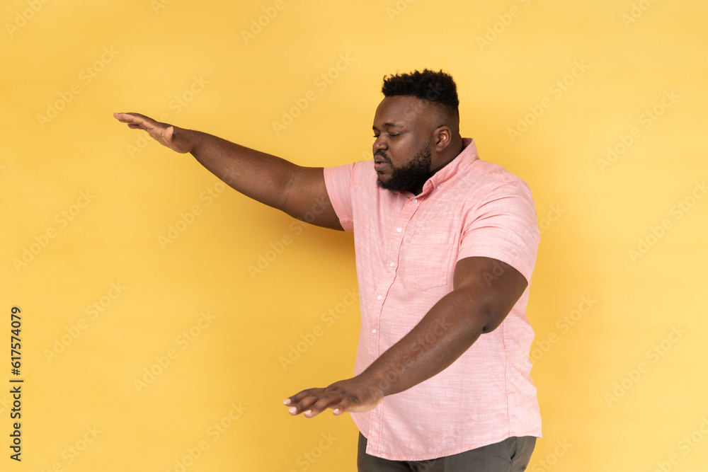 Side view of lonely blind disabled man wearing pink shirt standing with closed eyes and outstretched hands searching way, walking with doubts. Indoor studio shot isolated on yellow background. Side view of lonely blind disabled man wearing pink shirt standing with closed eyes and outstretched hands searching way, walking with doubts. Indoor studio shot isolated on yellow background.