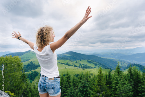 Young woman standing on cliff's edge and looking to a sky with raised hands