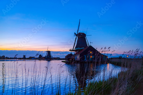Evening River Zaan with Dutch windmills in Zaandam, Netherlands. Sunset landscape with windmills and field wild herbs and flowers. Sunset landscape with windmills and field wild herbs and flowers. photo