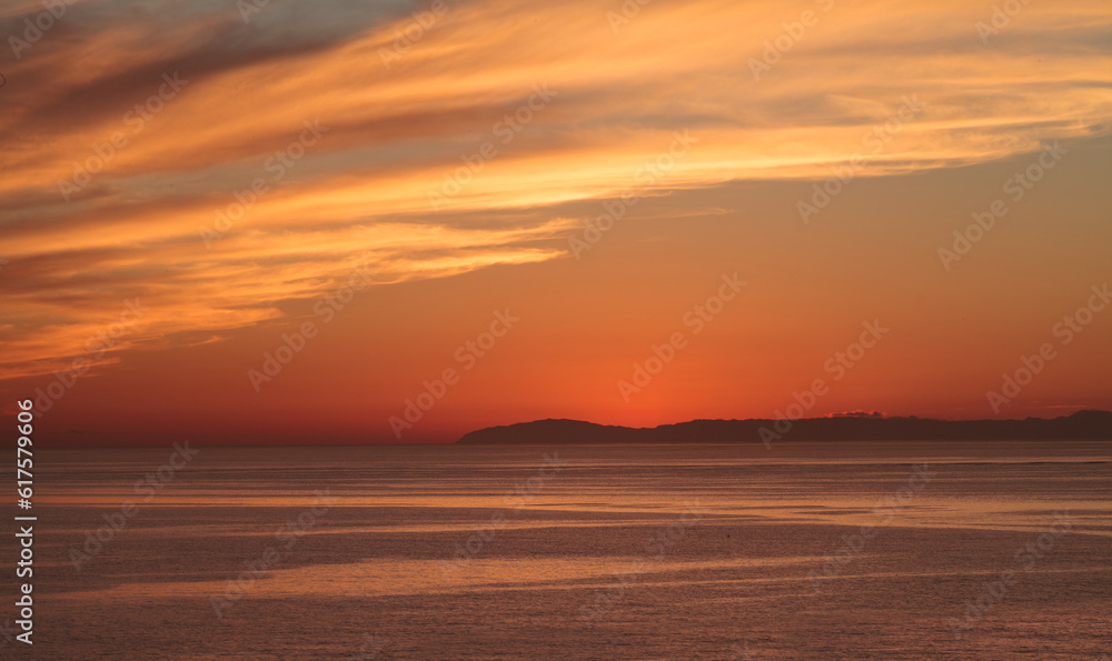 Orange sunset over Catalina Island in a calm ocean in Laguna Beach, Southern California, United States