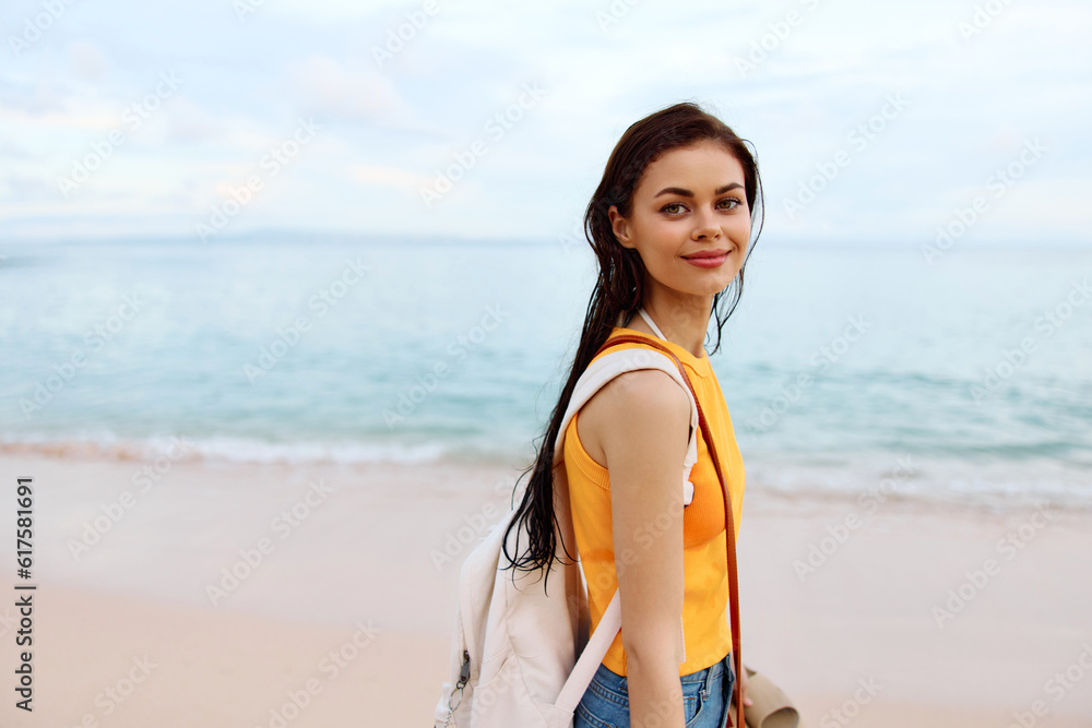 Young woman smile with teeth after swimming in the ocean with a backpack in wet clothes walking along the beach, summer vacation on the island by the ocean in Bali sunset Young woman smile with teeth after swimming in the ocean with a backpack in wet clothes walking along the beach, summer vacation on the island by the ocean in Bali sunset