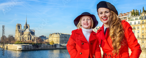 Bright in Paris. Portrait of smiling stylish mother and child tourists in red coats on embankment near Notre Dame de Paris in Paris, France photo