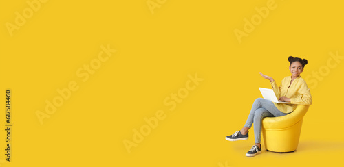 African-American girl with laptop sitting in armchair on yellow background with space for text