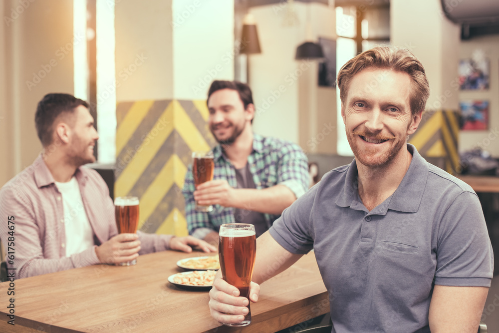 Pizza time. Friends spending time together in restaurant. Guys drinking beer and eating pizza. One man smiling and looking at camera