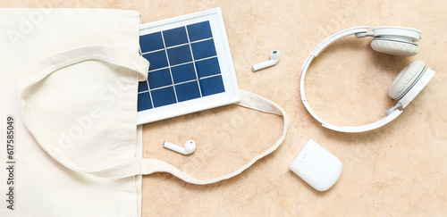 Bag with portable solar panel, wireless earphones and headphones on grunge background