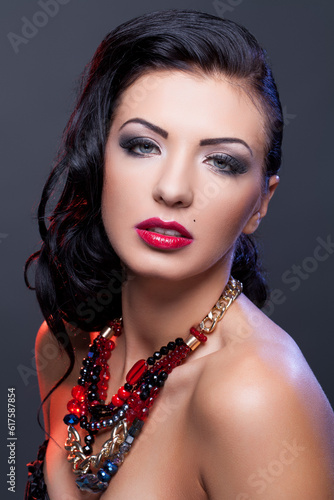Beautiful brunette young woman with bright make-up and red lips wearing necklace. Copy space.