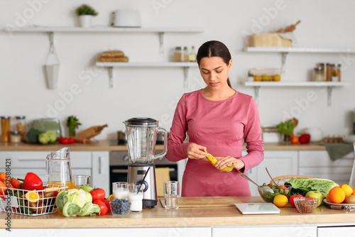 Sporty young woman peeling banana in kitchen