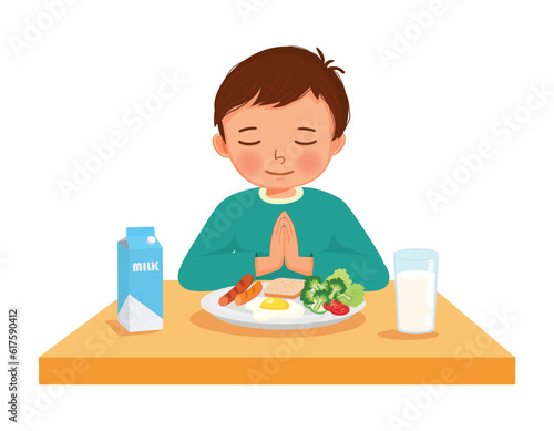 little boy praying before eating breakfast at the table