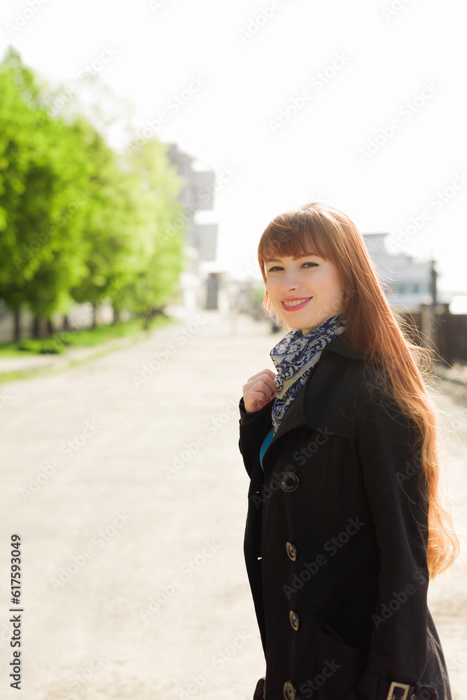 Beautiful red-haired young woman dressed in a stylish coat, walking down the embankment on a sunny day, examining the neighborhood. The concept of people, travel, tourism and lifestyle Beautiful red-haired young woman dressed in a stylish coat, walking down the embankment on a sunny day, examining the neighborhood. The concept of people, travel, tourism and lifestyle