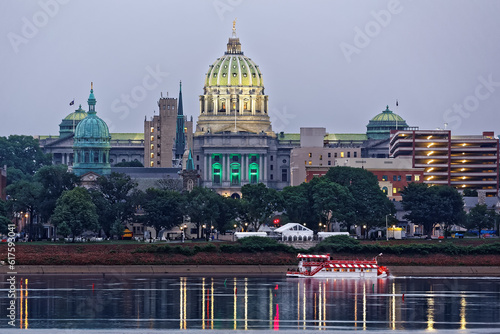Harrisburg Pennsylvania skyline with State Capital Building and a river boat in the foreground. Tents are set up in the park for Memorial Day festivities. The view is from across the Susquehanna River