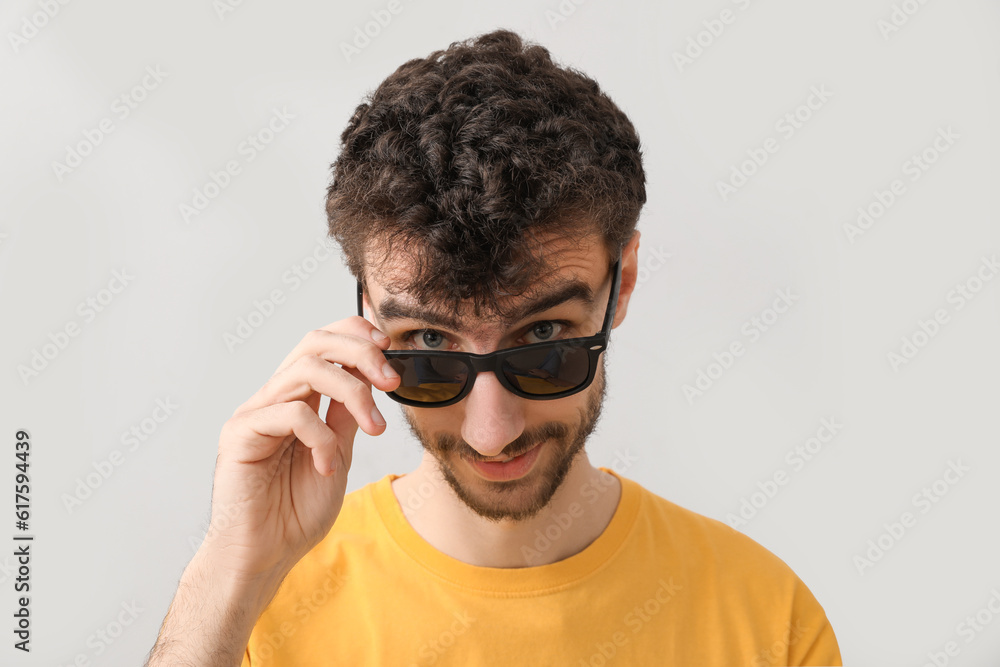 Young brunette man in sunglasses on light background, closeup Young brunette man in sunglasses on light background, closeup