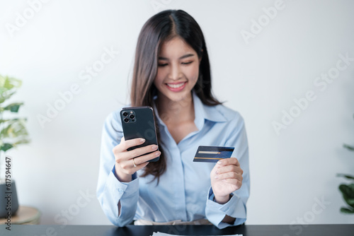 Beautiful Asian woman with smart phone and credit card, she fills in credit card information to pay for goods and services, online shopping concept pay by credit card via smartphone.