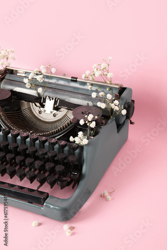 Vintage typewriter with gypsophila flowers on pink background, closeup