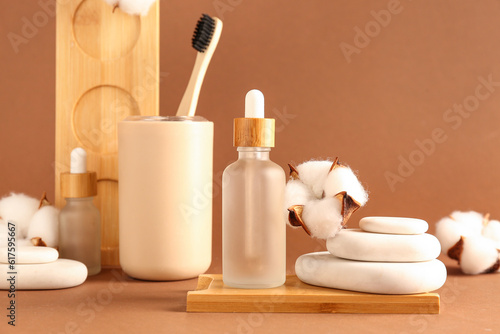 Bottles of essential oil, toothbrush, spa stones and cotton flowers on color background