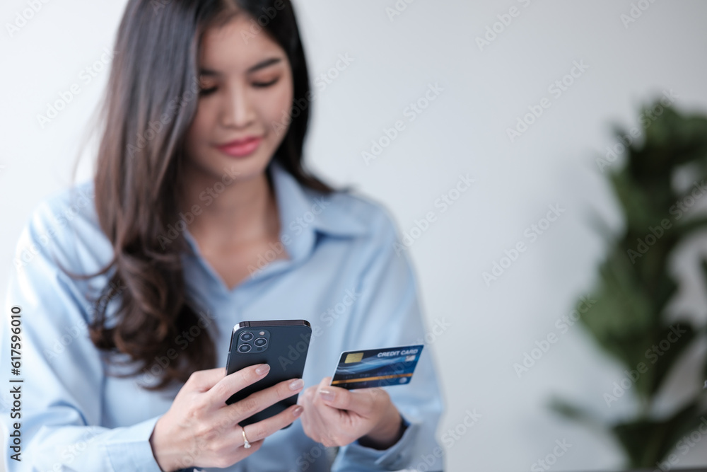 Close up Asian woman with smart phone and credit card, she fills in credit card information to pay for goods and services, online shopping concept pay by credit card via smartphone.