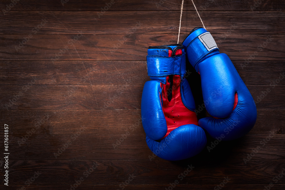 A pair of bright blue and red boxing gloves hangs against wooden background. Boxing backgrounds and still-life. Colorful accessories for sport. Horizontal photo. Training and sportive exercise. Concep