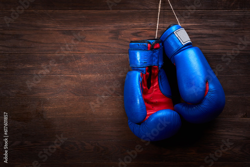 A pair of bright blue and red boxing gloves hangs against wooden background. Boxing backgrounds and still-life. Colorful accessories for sport. Horizontal photo. Training and sportive exercise. Concep © Designpics