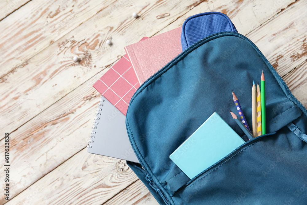 Naklejka premium Blue school backpack with notebooks and pencils on wooden background